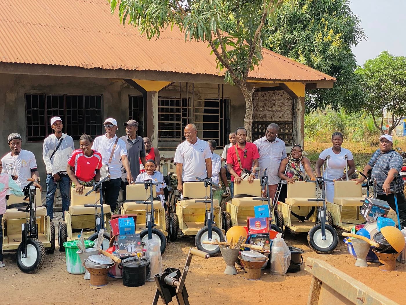 Recipients of hand-cranked mobility tricycles gathered with WESOFOD-SL staff in front of a community building