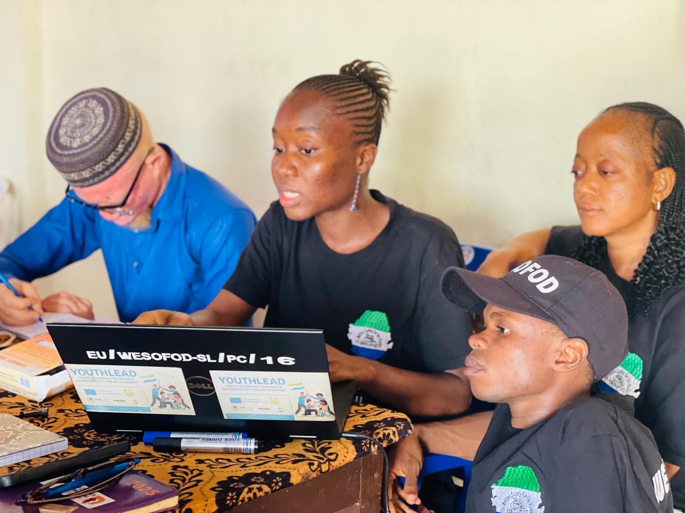 WESOFOD-SL staff working together at a laptop with YOUTH LEAD materials on the screen