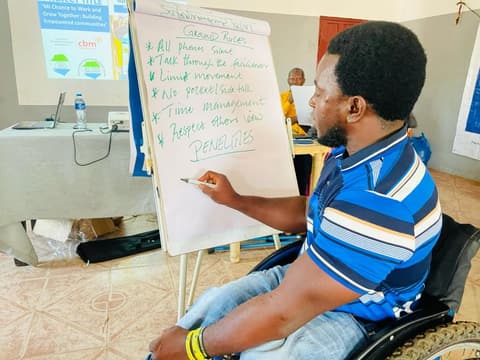 A participant in a wheelchair writes the training ground rules onto a flip chart at the National Disability Inclusion Training.
