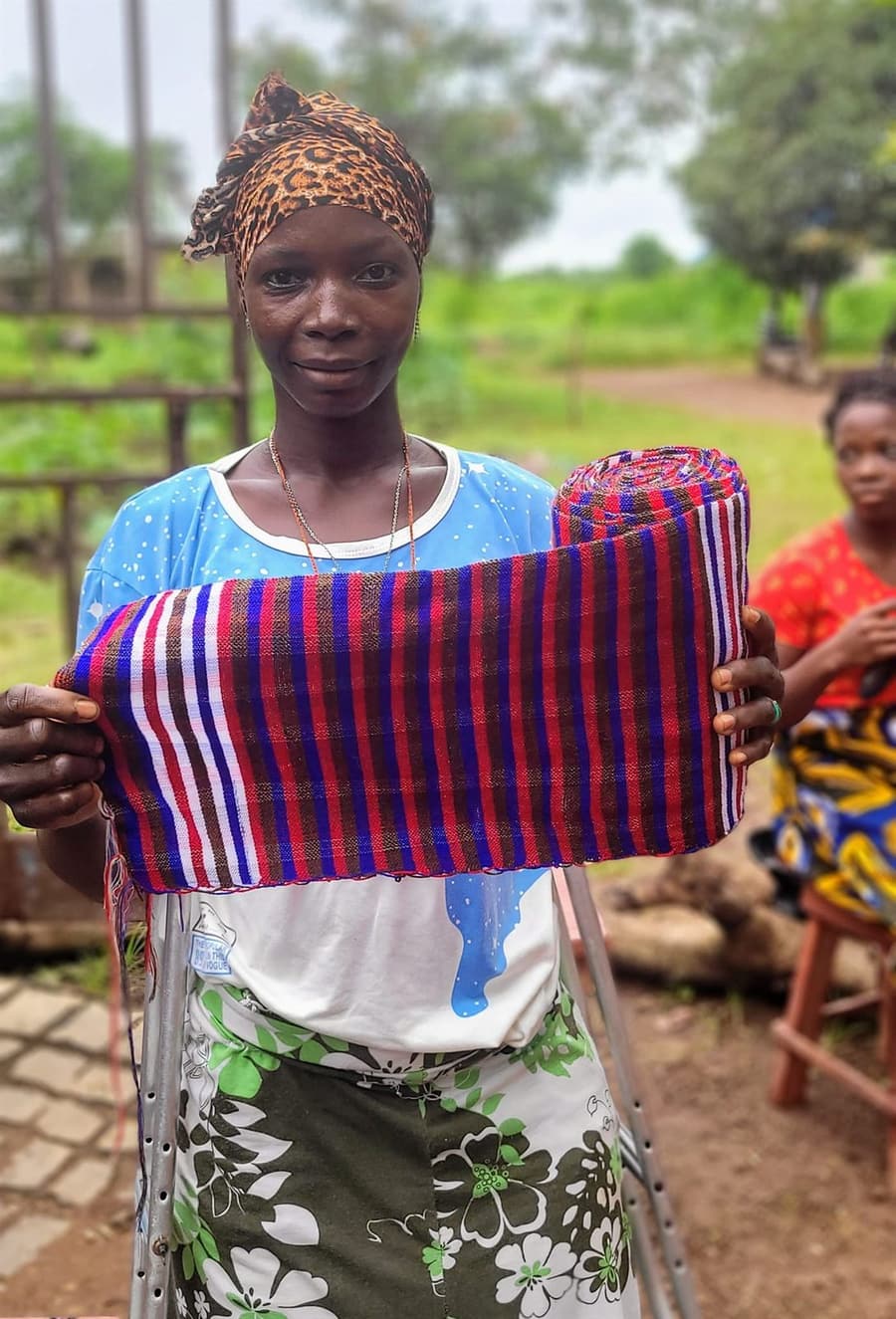 A young woman holding up a length of finished striped cloth she has woven